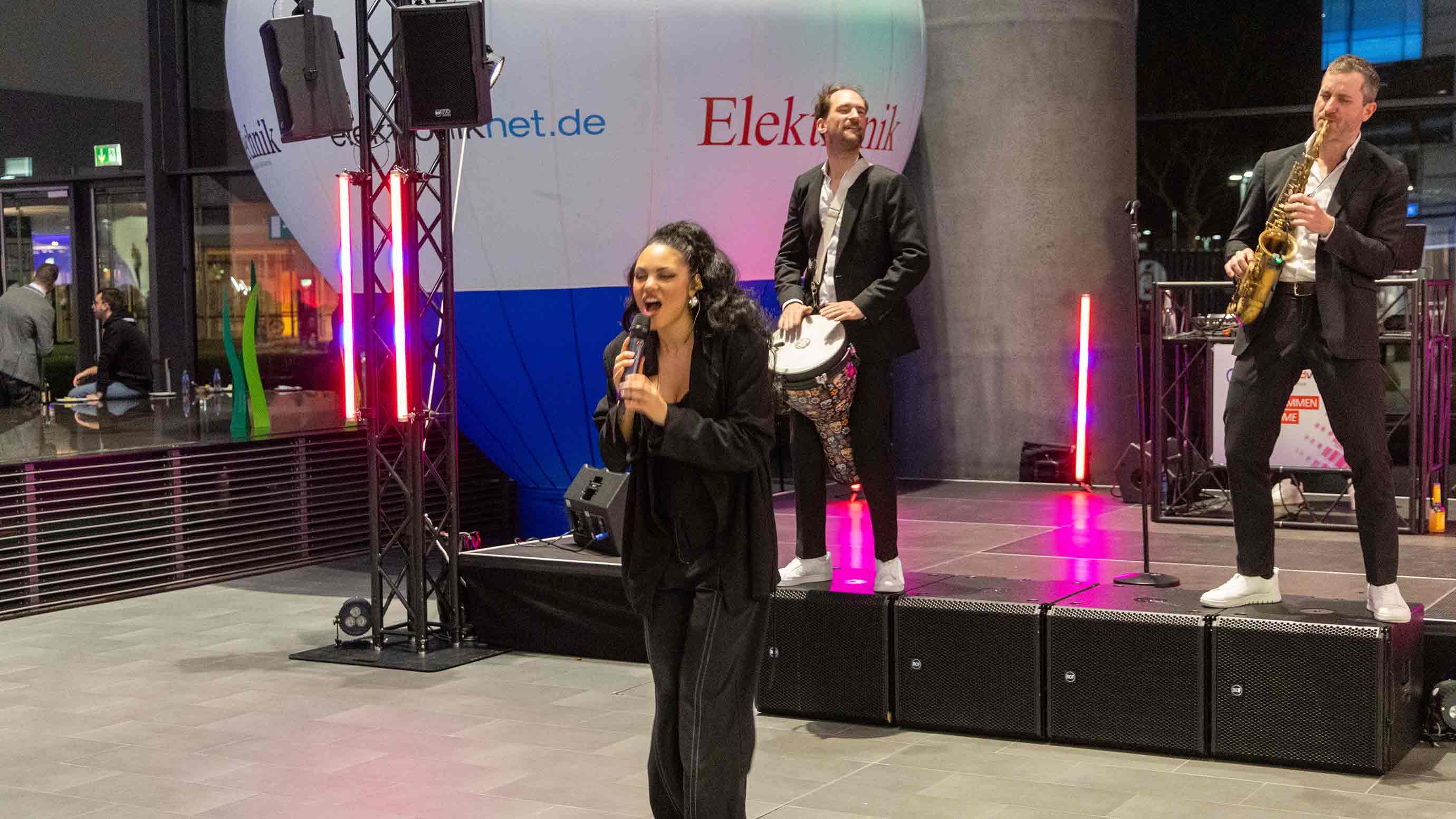 Live music performance with vocals and instruments on a stage inside an exhibition hall.